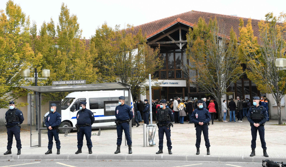 French CRS police officers stand as adults and children gather in front of flowers displayed at the entrance of a middle school in Conflans-Sainte-Honorine, 30kms northwest of Paris, on October 17, 2020, after a teacher was beheaded by an attacker who has been shot dead by policemen. (AFP)