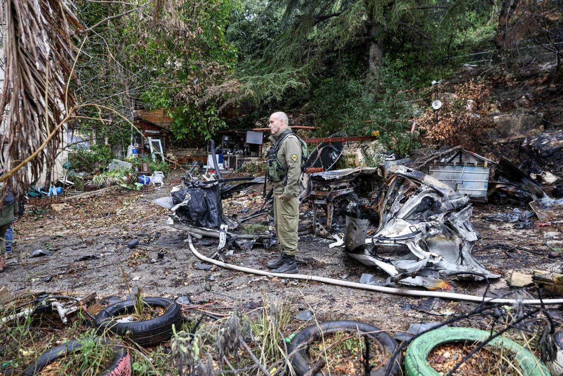 A soldier stands near a car destroyed in a strike by Lebanon’s Hezbollah movement in Kibbutz Manara in northern Israel near the Lebanon border, on Nov. 27, 2023. (AFP)