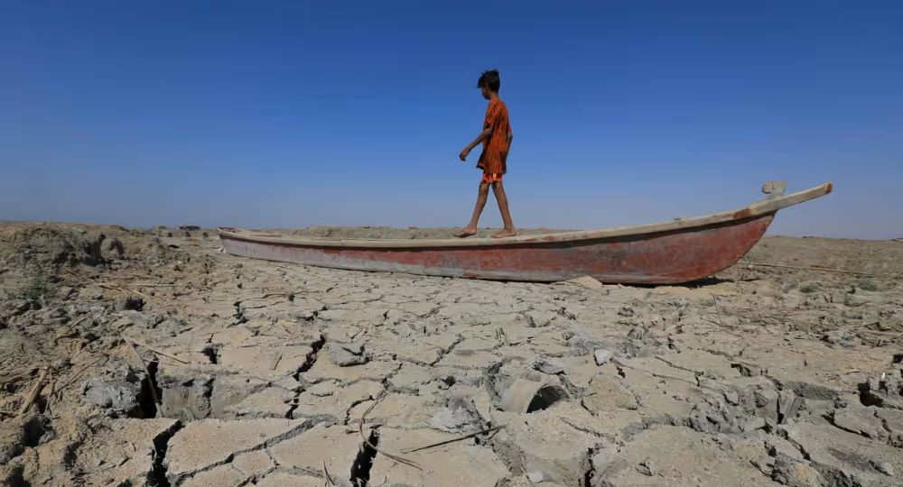 A boy walks on a boat left lying on the dried-up bed of a section of Iraq's receding southern marshes, June 2022. (AFP)