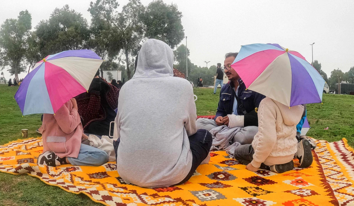 People sit with umbrellas along a promontory in al-Namas in Saudi Arabia's Asir province, on August 16, 2022. (AFP)