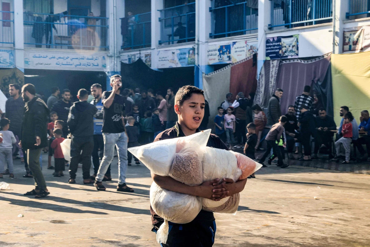 A boy walks with sacks of food supplies through a yard at a school run by the United Nations Relief and Works Agency for Palestine Refugees in the Near East (UNRWA) in Rafah in the southern Gaza Strip on November 14, 2023, where internally displaced Palestinians have taken refuge amid ongoing battles between Israel and the Palestinian militant group Hamas. (AFP)
