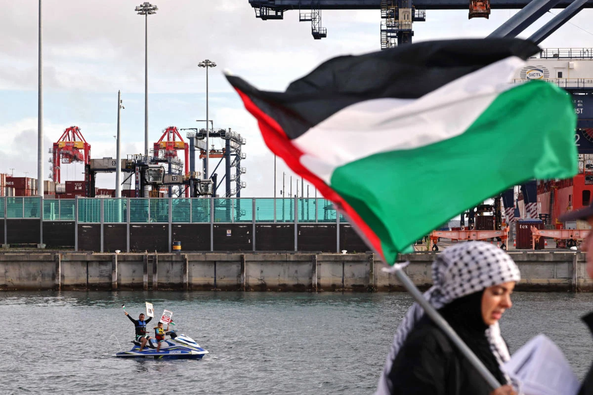 A member of the Australian Palestinian community holds a Palestinian flag as others hold placards while on a jet ski during a protest at the Port Botany terminal in Sydney on November 21, 2023. (AFP)
