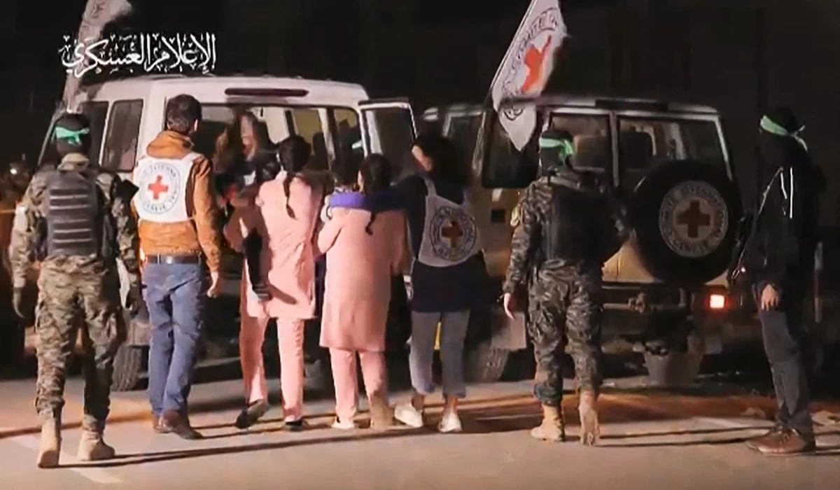 An image grab from a handout video released by the Hamas Media Office shows Hamas fighters accompanying newly released Israeli hostages (in pink) to a Red Cross vehicle, in the Gaza Strip on November 27, 2023. (AFP)