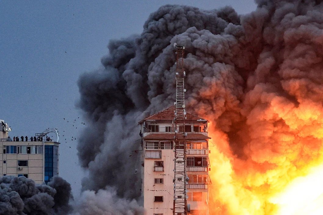 People standing on a rooftop watch as fire and smoke rises above a building in Gaza City during an Israeli air strike. (AFP)