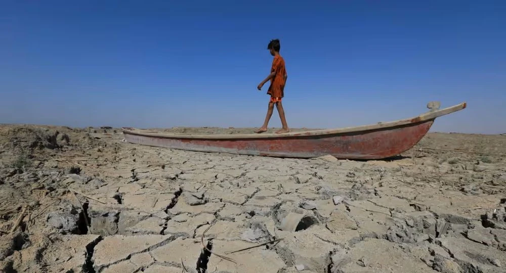 A boy walks on a boat left lying on the dried-up bed of a section of Iraq's receding southern marshes, June 2022. (AFP)