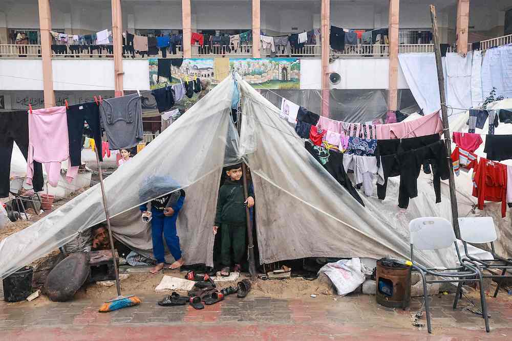 Palestinian boys stand in their makeshift tent at a camp set up on a schoolyard in Rafah on Dec. 13, 2023. (AFP)