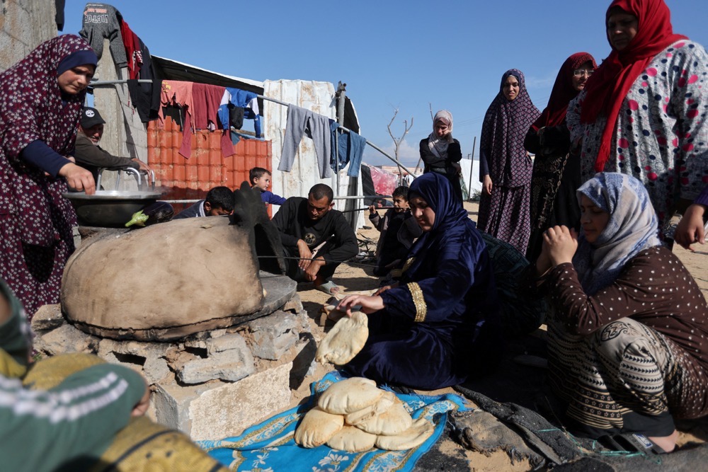 People wait while a woman prepares food, as displaced Palestinians, who fled their houses due to Israeli strike, shelter in a camp in Rafah. (Reuters)