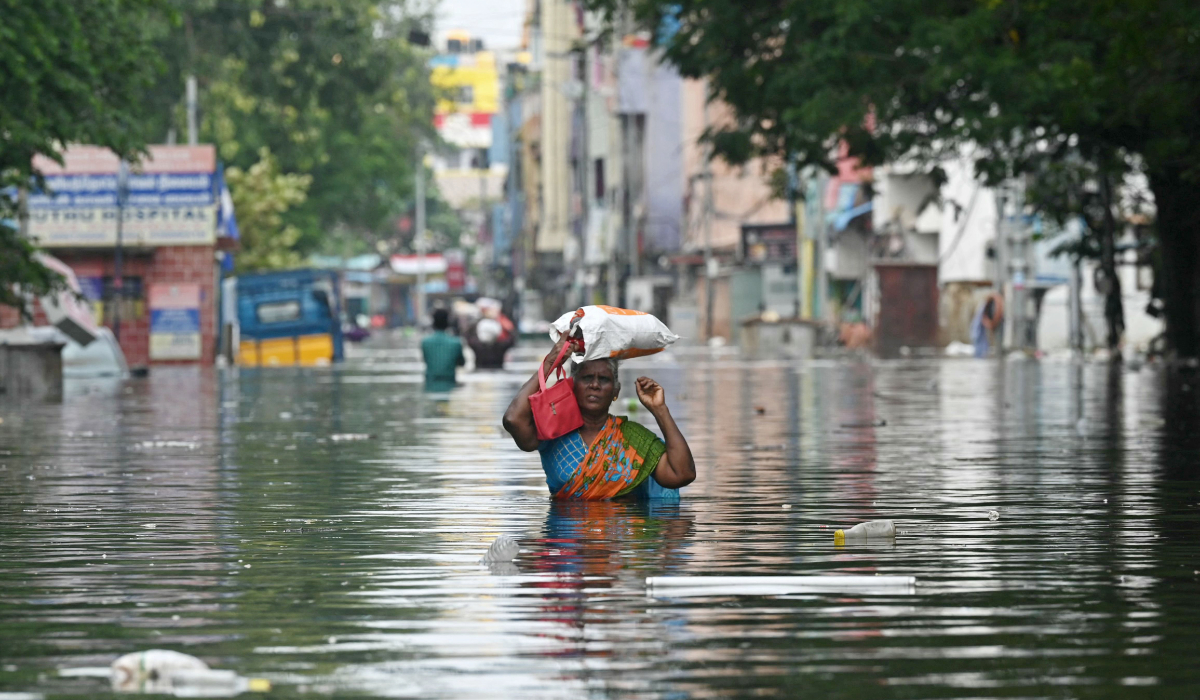 A woman along with her belongings, wades through a flooded street after heavy rains in Chennai on December 6, 2023. (AFP)