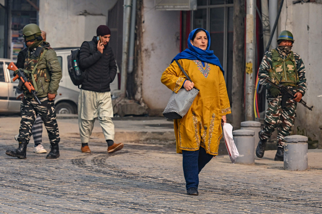 People walk along a street as Indian paramilitary personnel patrol in Srinagar on Dec. 11, 2023, ahead of Supreme Court's verdict on Article 370. (AFP)