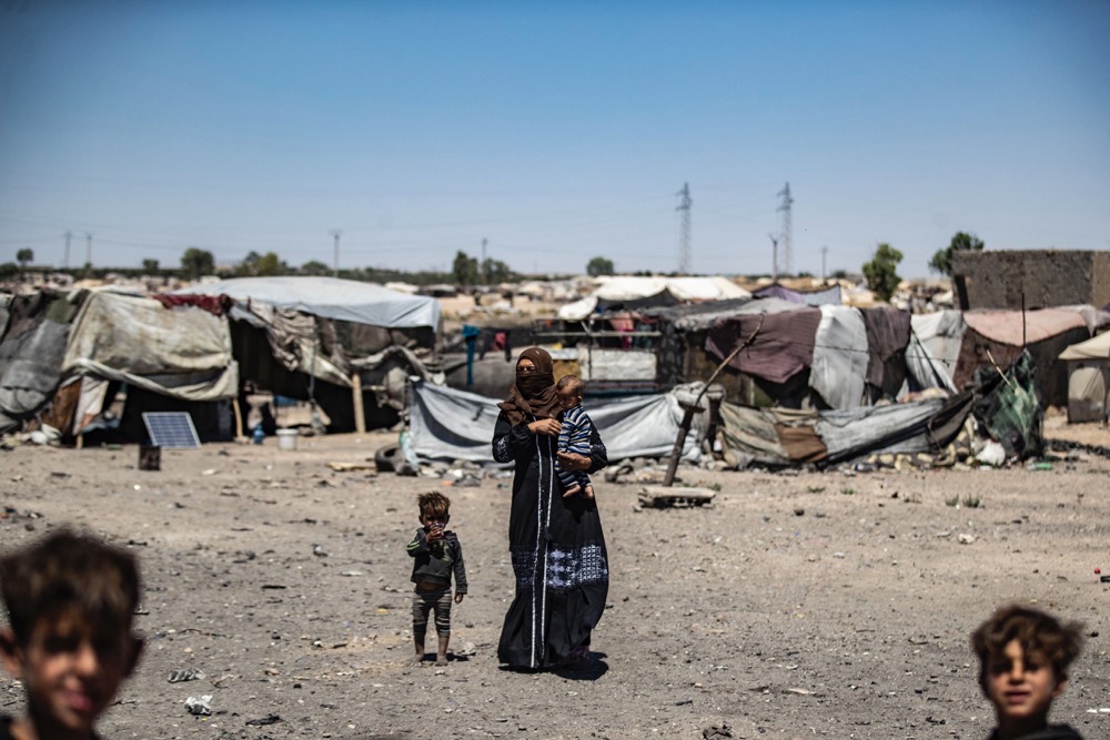 People stand near tents at the Sahlat Al-Banat makeshift camp for internally displaced people set-up next to a waste dump on the outskirts of the northern Syrian city of Raqqa, on July 10, 2023. (AFP)