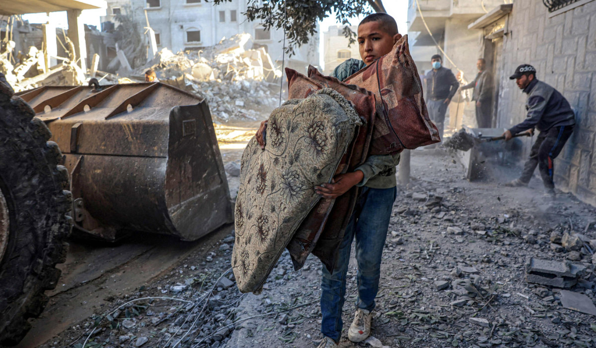 A Palestinian boy carries pillows as a tractor clears debris of destroyed buildings in the southern Gaza Strip on Friday amid continuing battles between Israel and Hamas. (AFP)