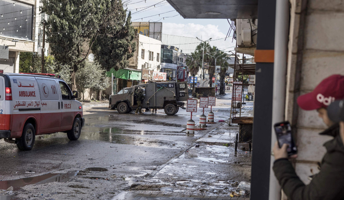 Palestinian youths observe an Israeli army patrol car from the safety of a corner at the entrance of the Jenin refugee camp in the occupied West Bank on December 13, 2023, as battles continue between Israel and the militant movement Hamas in Gaza. (AFP)