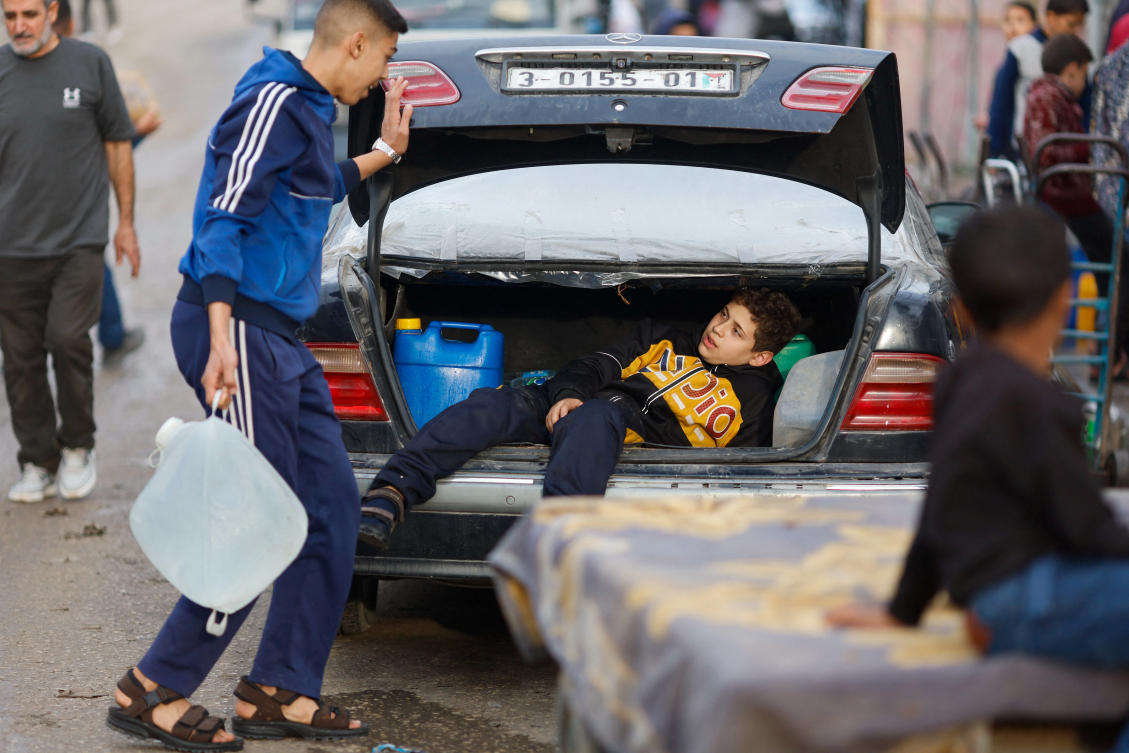 A boy lies in a vehicle’s trunk as Palestinians gather to unload boxes with bottles of water from trucks, amid drinking water shortages, at Rafah border with Egypt on Dec. 17, 2023. (Reuters)