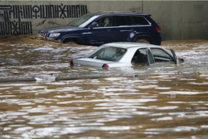 A man, background, drives his car in front a car submerged in flood water at a highway flooded by the rains, in Beirut on Dec. 23, 2023. (AP)