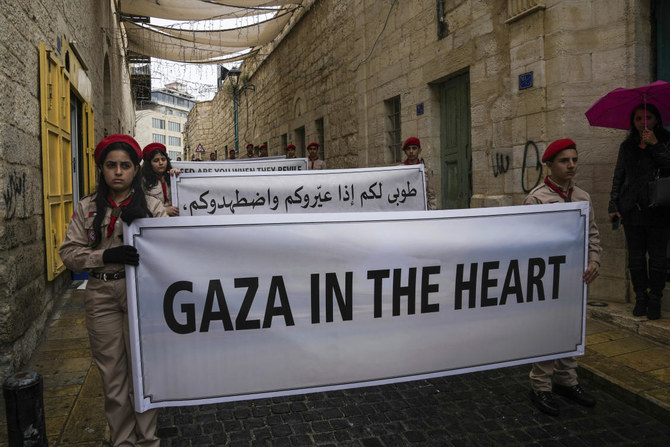 Palestinian scouts hold signs in solidarity with Palestinians in the Gaza Strip calling to end the Israel-Hamas war, near the Church of the Nativity, traditionally believed to be the birthplace of Jesus, on Christmas Eve in the West Bank city of Bethlehem, on December 24, 2023. (AP)