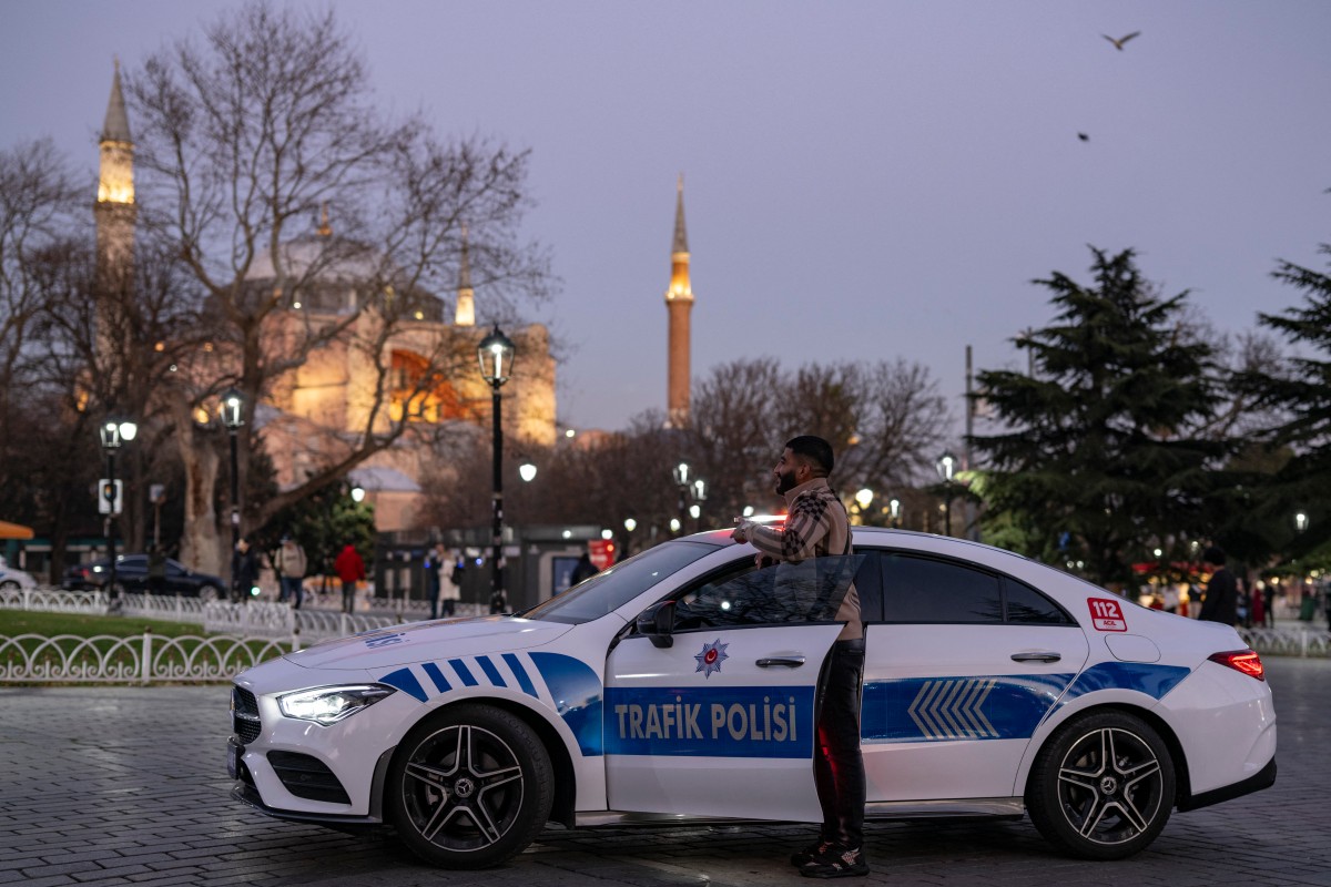 A man poses for a photograph next to a Mercedes converted into a police vehicle, on display at Hagia Sophia Square in Istanbul on December 27, 2023. (AFP)