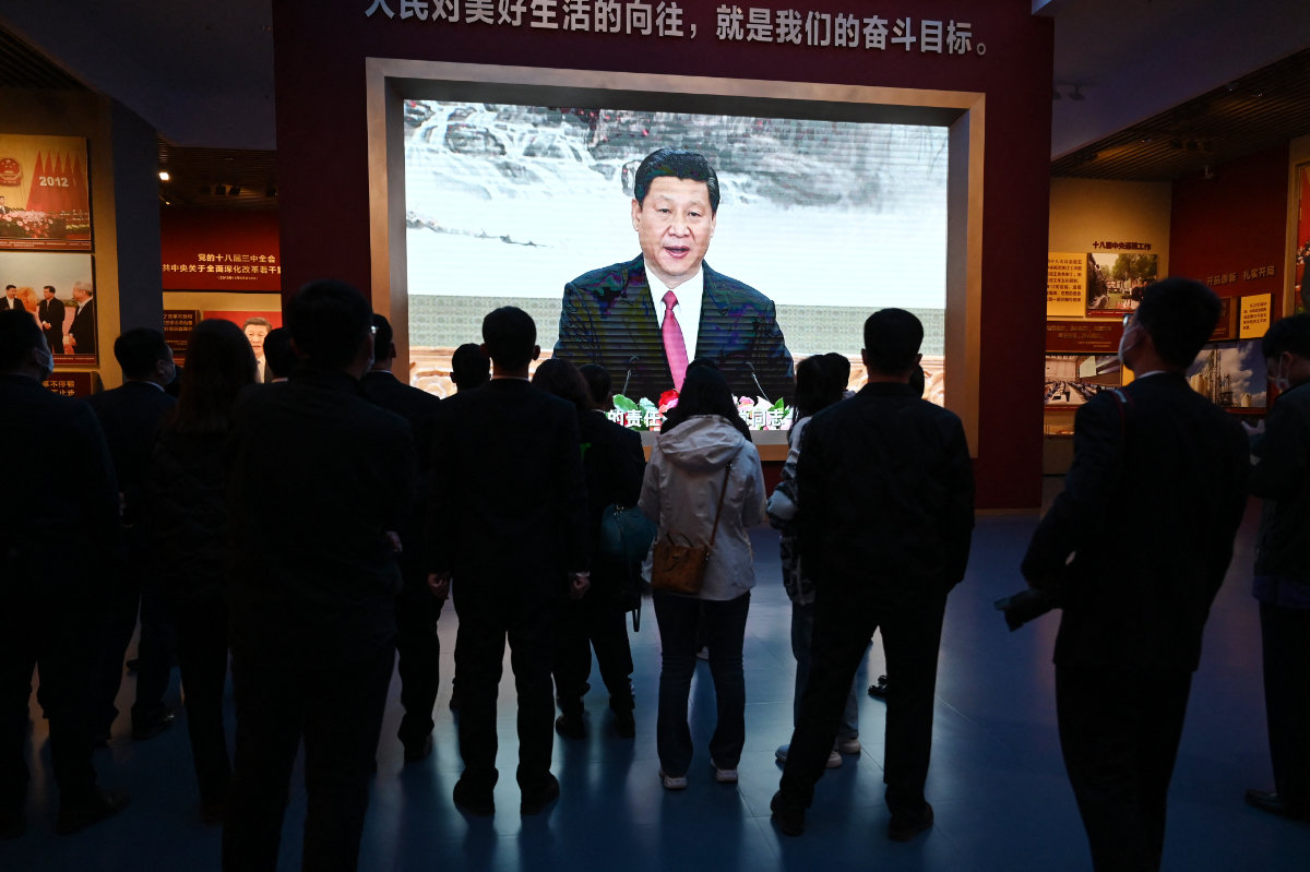 People walk past a video screen showing a speech by Chinese President Xi Jinping at the Museum of the Communist Party of China in Beijing on March 3, 2023. (AFP/File)