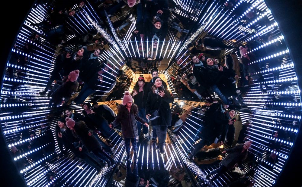 People stand in a giant kaleidoscope, an installation by French artist Guillaume Marmin, during the Festival of Lights (Fete des Lumieres), Lyon, France, Dec. 7, 2023. (AFP)
