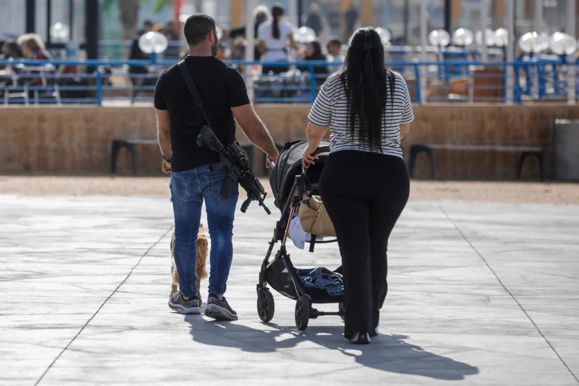 An armed Israeli man walks with his family in the northern coastal Israeli city of Nahariya near the border with Lebanon on Dec. 8, 2023. (AFP)