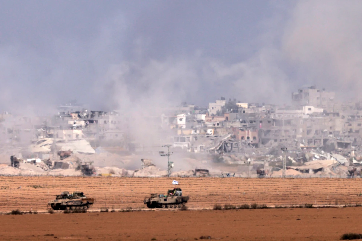 A picture taken from southern Israel near the border with the Gaza Strip on Dec. 10, 2023, shows Israeli armored personnel carriers driving along the border fence as smoke rises above the Palestinian enclave amid ongoing battles with the Palestinian Hamas militant group. (AFP)