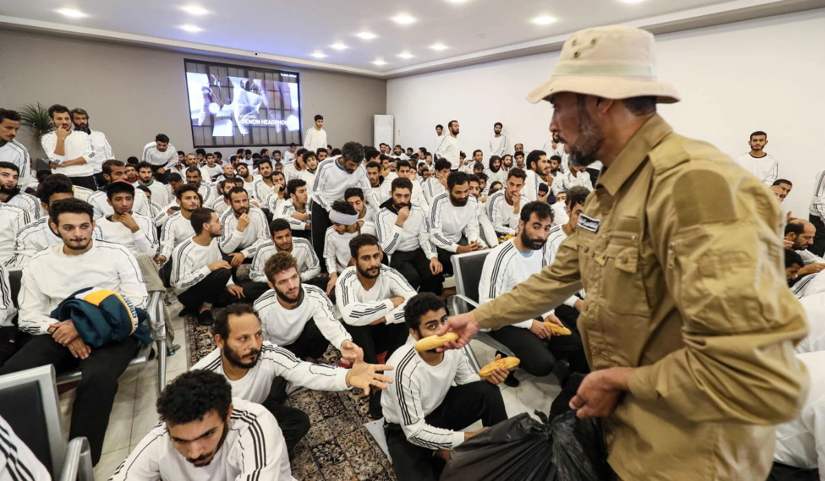 Egyptian migrants receive bread as they await processing during a deportation operation by the Tripoli-based government in the Libyan capital on December 12, 2023. (AFP)