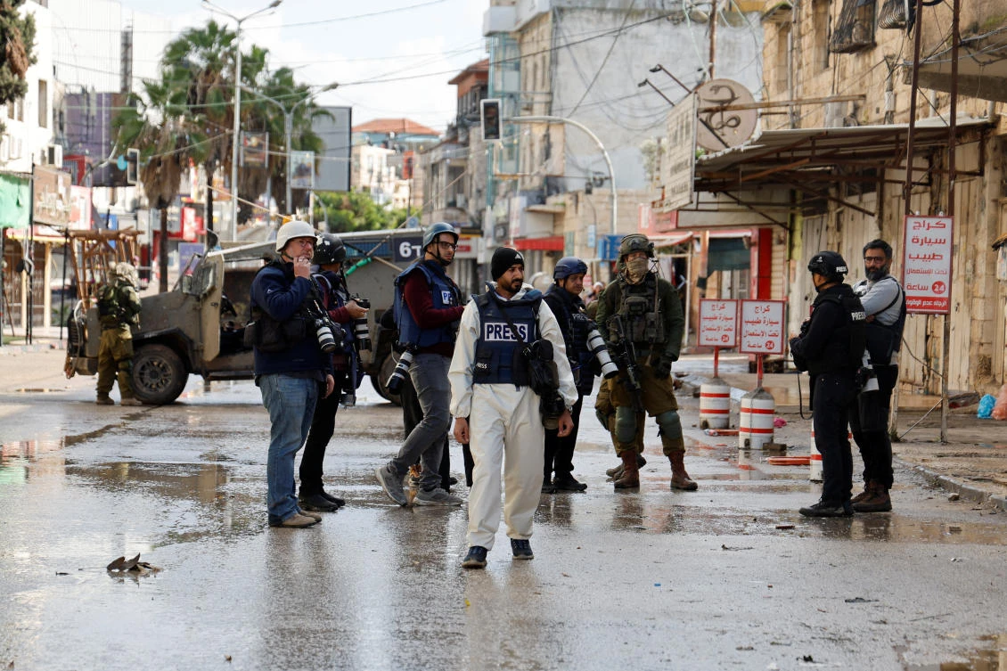 Journalists gather as Israeli military vehicles block the road during a raid in Jenin in West Bank on Dec. 13, 2023. (Reuters)