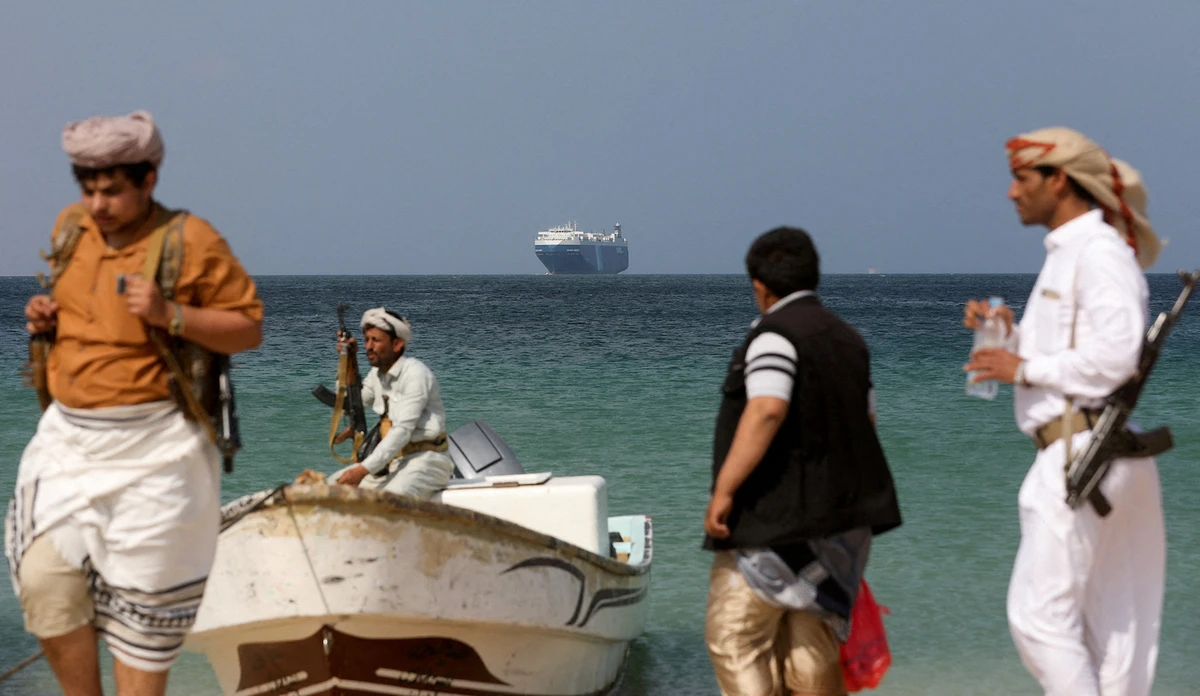 Armed men stand on the beach as the Galaxy Leader commercial ship, seized by Yemen’s Houthis in November, is anchored off the coast of Al-Salif, Yemen. (File/Reuters)