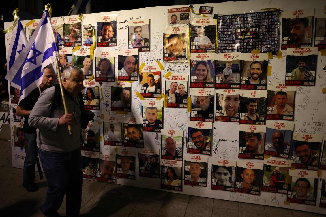 Israeli men with national flags walk past a wall bearing portraits of Israeli hostages held in Gaza since the October 7 attacks by Hamas, on the sidelines of a rally calling for their release, in Tel Aviv on Jan. 6, 2024. (AFP)