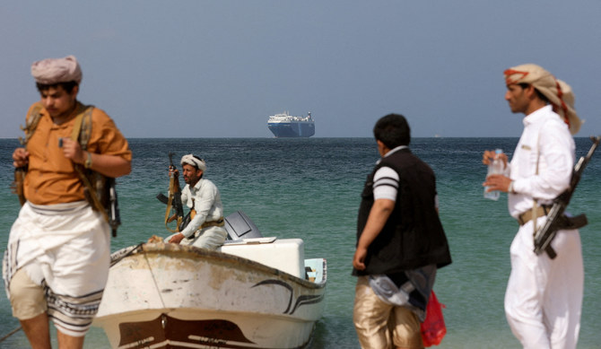 Armed men stand on the beach as the Galaxy Leader commercial ship, seized by Yemen’s Houthis in November, is anchored off the coast of Al-Salif, Yemen. (File/Reuters)