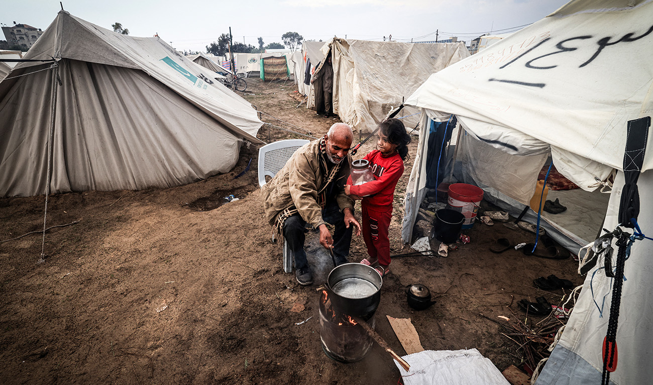 A Palestinian man prepares food for his family outside his tent at a camp for displaced people in Rafah, in the southern Gaza Strip where most civilians have taken refuge, on December 13, 2023. (AFP)