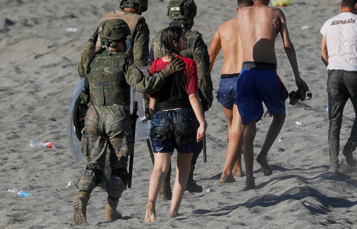 A female migrant is led by a Spanish female soldier as she is deported to Morocco after she crossed the border swimming from Morocco to Spain, at El Tarajal beach, after thousands of migrants swam across this border during last days, in Ceuta, Spain, May 19, 2021. Picture taken May 19, 2021. (REUTERS)