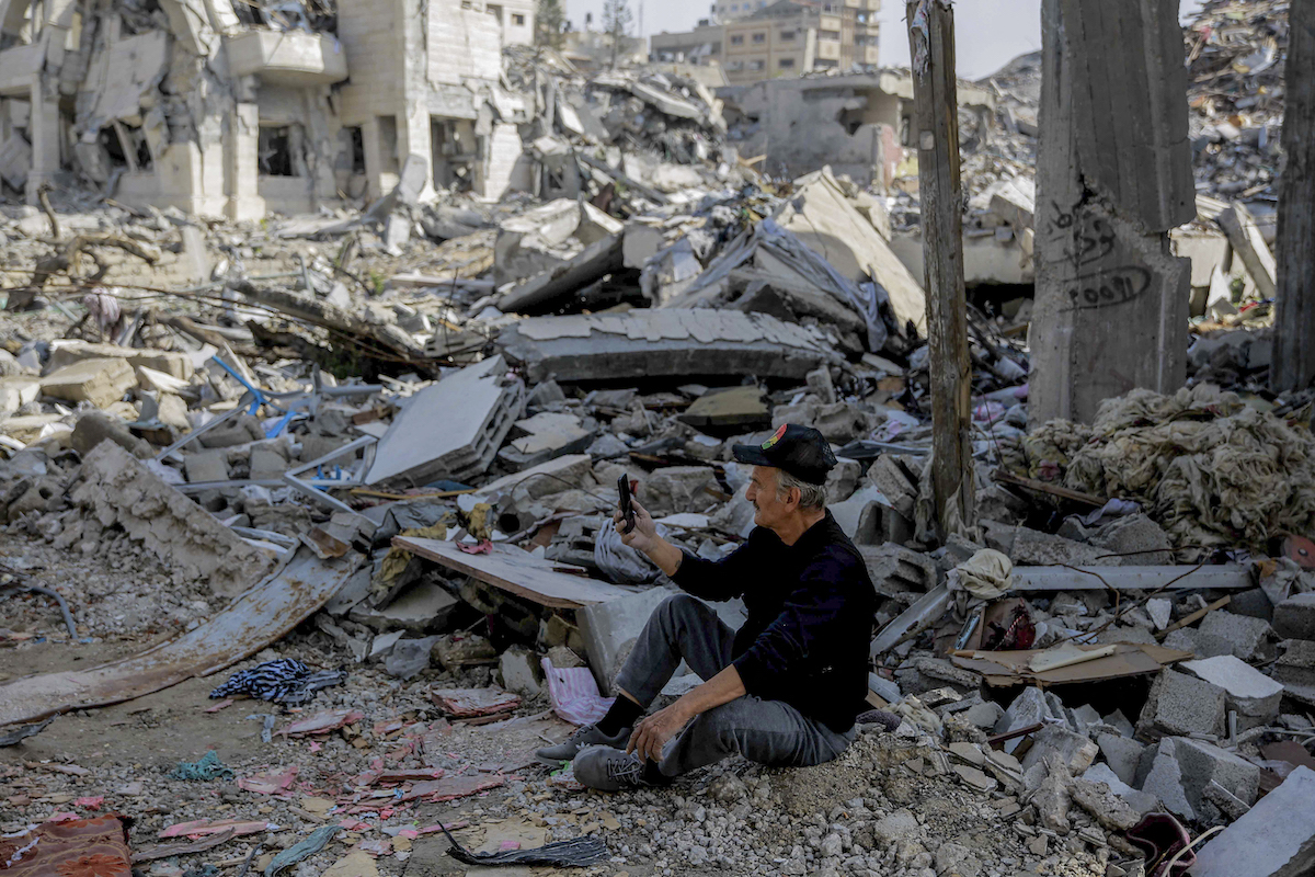 A Palestinian man uses his phone as he sits amid the rubble of destroyed buildings in Gaza City. (File/AFP)