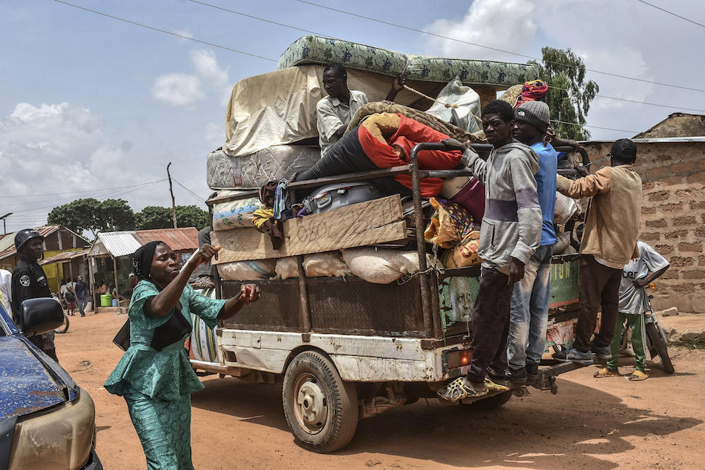 Above, residents hang from the back of a pick-up truck on May 20, 2023 after fleeing unrest in central Nigeria. (AFP)