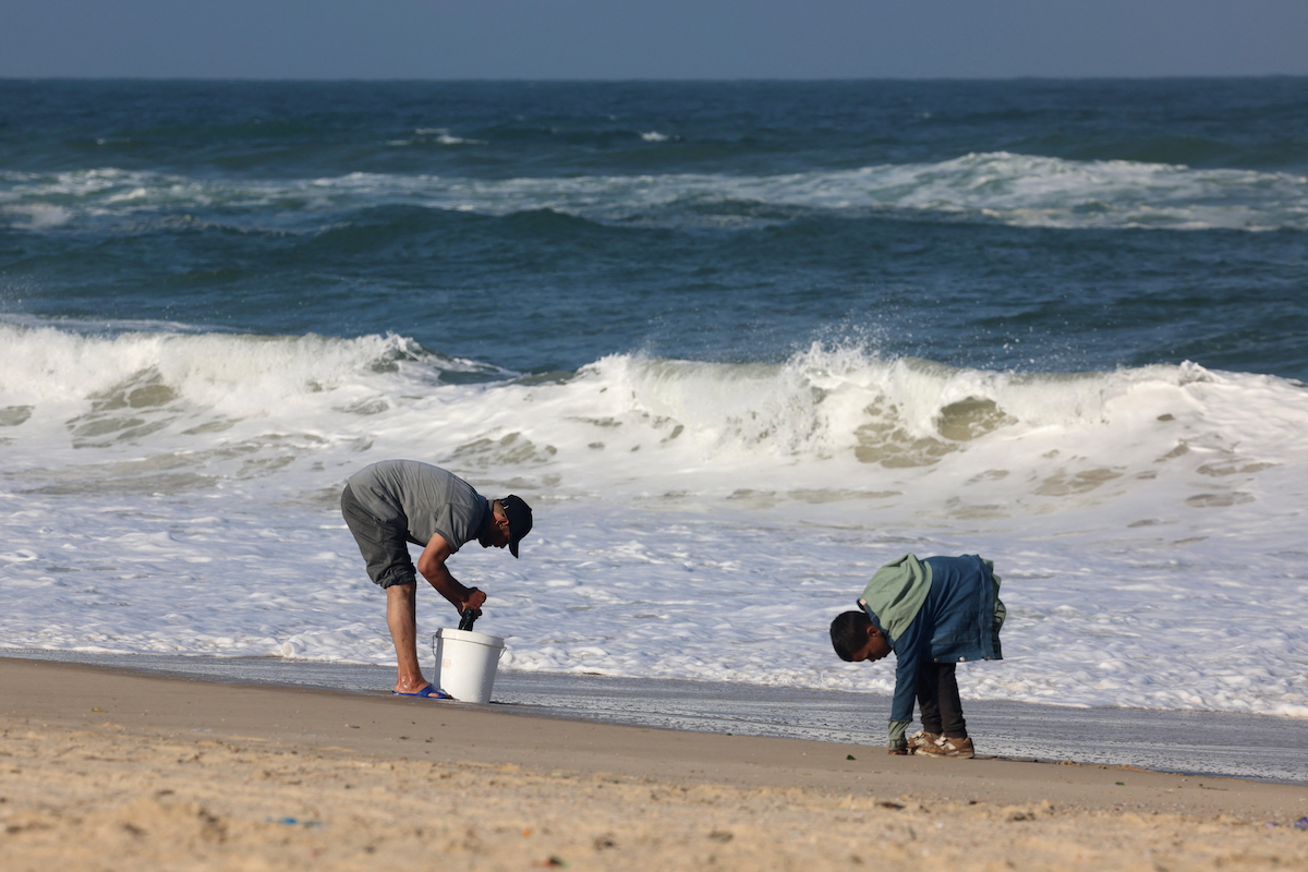 People wash garments in sea water at a makeshift tent camp for displaced Palestinians in Rafah near the border with Egypt in the southern Gaza Strip. (File/AFP)