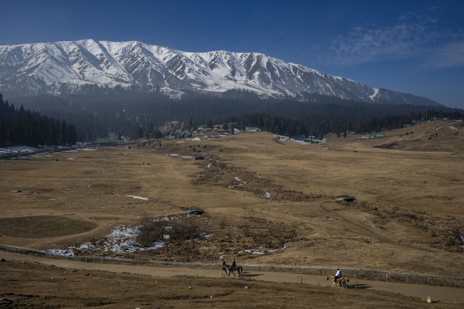 Tourists take a horse ride on grassy, snowless ski slopes in Gulmarg in Indian-controlled Kashmir on Jan. 13, 2024. (AP Photo)