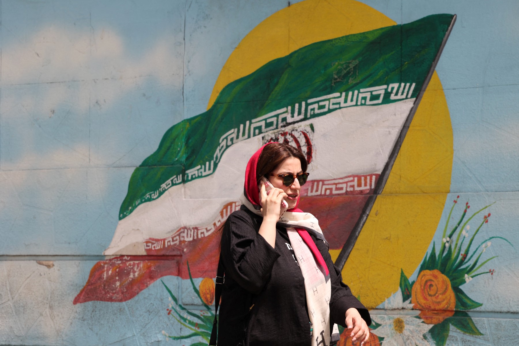 An Iranian woman walks past an Iranian flag painted on a wall in a street in Tehran on April 10, 2023. (AFP)