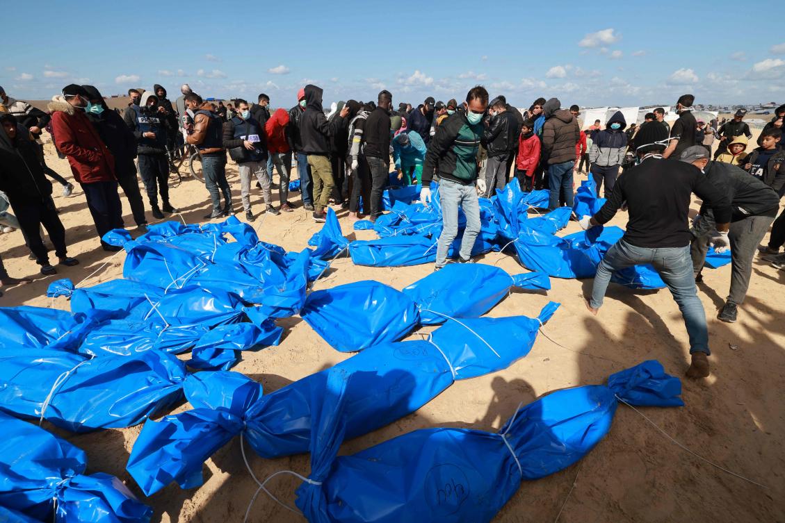 Civilians watch as Gaza-based Palestinian Health Ministry workers bury the bodies of unidentified Palestinians whose date of death is not known after they were returned by Israel earlier on the same day through the Kerem Shalom crossing, at a mass grave east of Rafah on Jan. 30, 2024. (AFP)