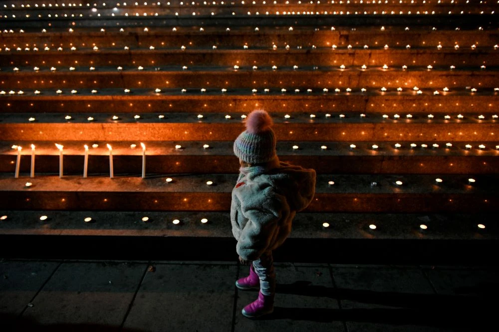 A child stands near lighted candles in front of the national theatre in Pristina, Kosovo, Jan. 15, 2024, to mark the 25th anniversary of the Racak Massacre. (AFP)