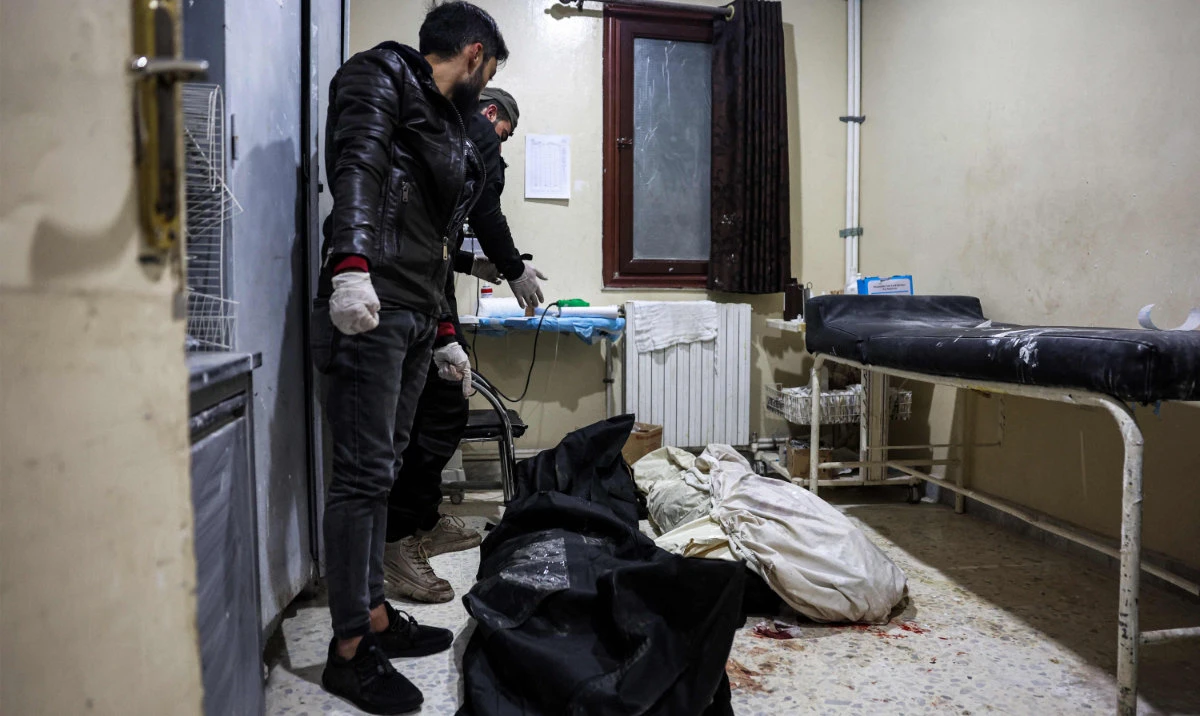 Men stand over the bodies of two victims who were killed in the aftermath of reported bombardment by Syrian government forces, at a hospital in the rebel-held city of Idlib in northwestern Syria on December 30, 2023. (AFP)