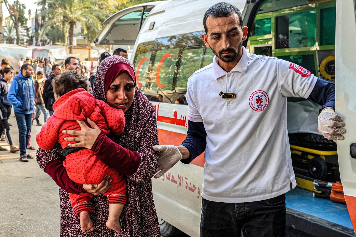 A paramedic assists a woman carrying a child arriving at the European Hospital in Khan Yunis in the southern Gaza Strip on December 31, 2023. (AFP)