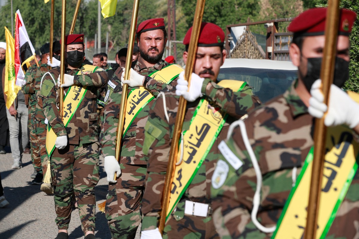 Fighters lift flags of Iraq and paramilitary groups, including al-Nujaba and Kataib Hezbollah, during a funeral in Baghdad for five militants killed in a US strike in northern Iraq in December (AFP)
