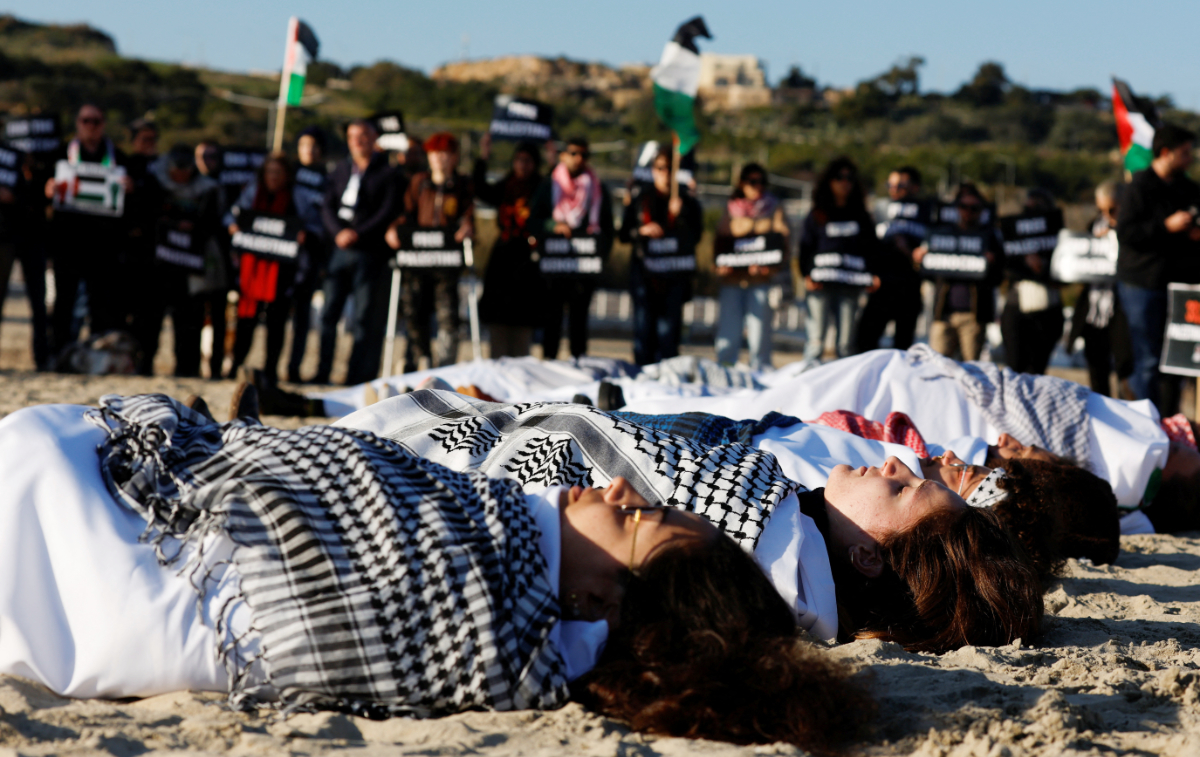 Activists wrapped in white sheets lie in the sand to highlight the death of civilians in Gaza during a symbolic protest in Mellieha, Malta. (REUTERS)