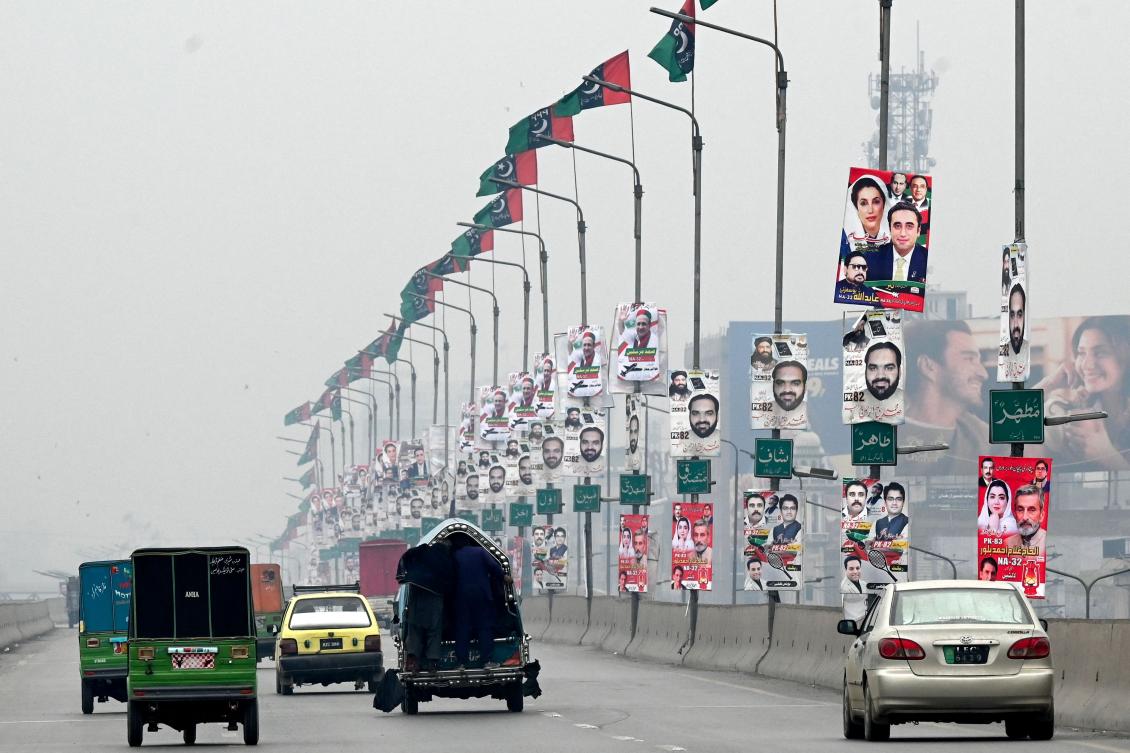 Commuters move past the election posters installed on light poles along a road in Peshawar ahead of the upcoming general elections. (File/AFP)