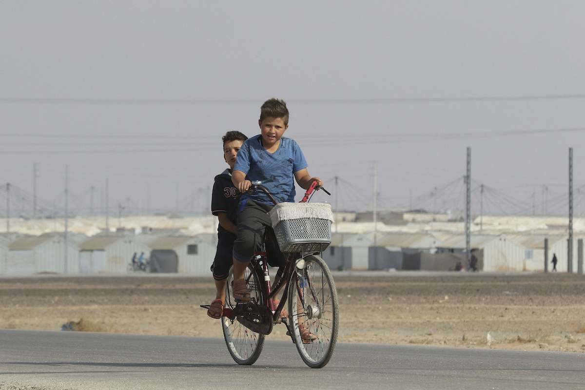 Young Syrian refugees ride a bicycle at the Azraq camp for Syrian refugees in northern Jordan on August 2, 2018. (File/AFP)