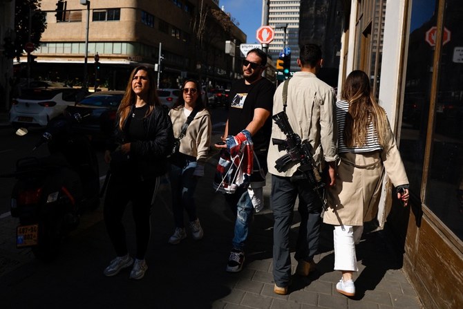 People walk past an off-duty Israeli soldier carrying an assault rifle, amid the ongoing conflict between Israel and Hamas, in Tel Aviv on February 9, 2024. (Reuters)