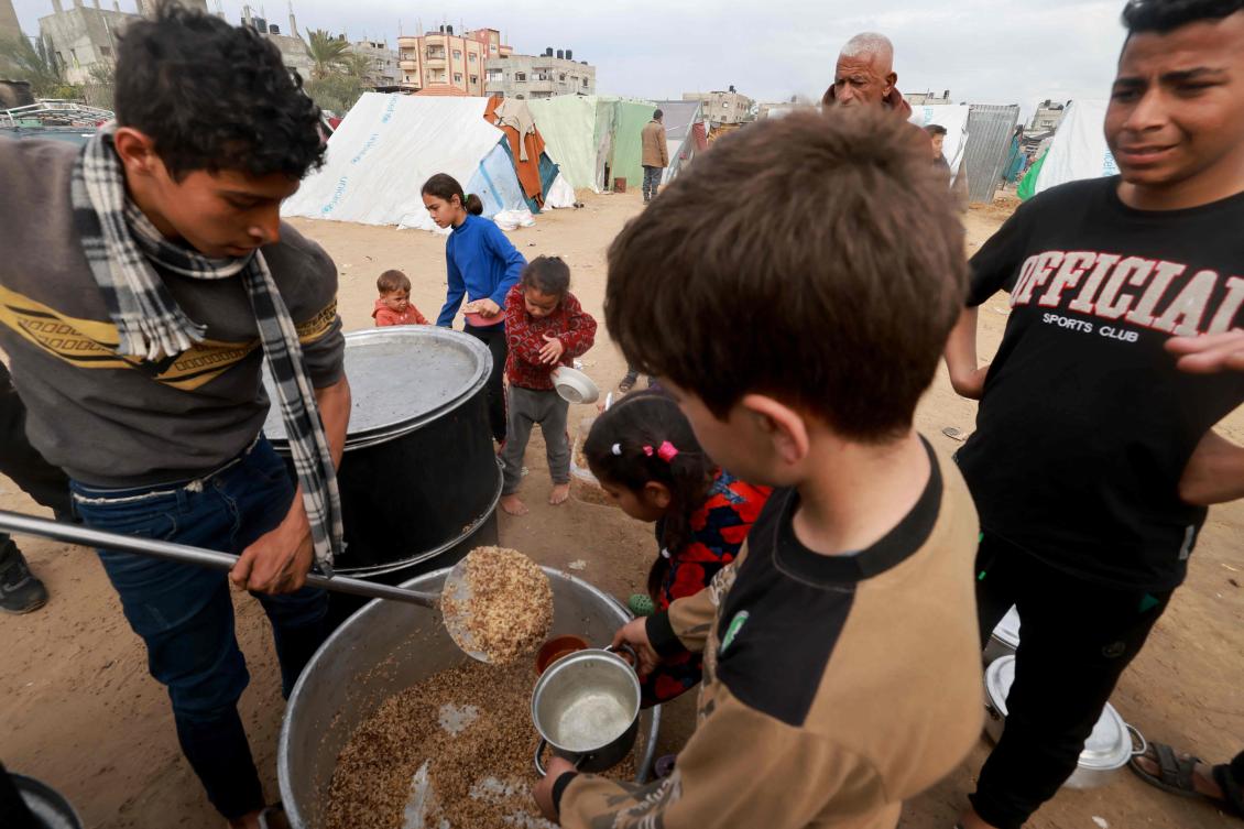 Palestinian children receive food cooked by a charity kitchen amid shortages of food supplies in Rafah on Feb. 13, 2024. (AFP)