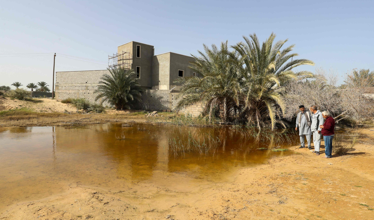 People stand next to a flooded plot of land in Libya’s coastal city of Zliten, 150 kilometers east of the capital, as a result of rising groundwater levels. (AFP)