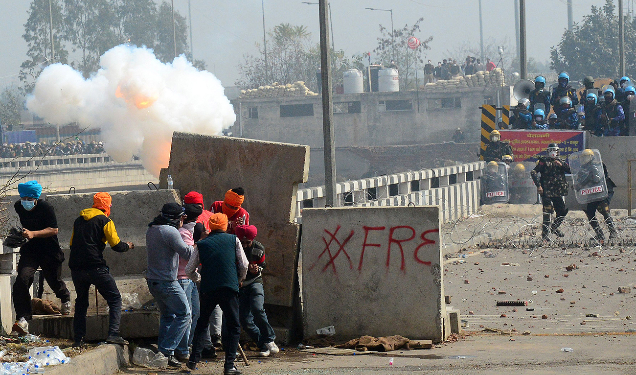 Farmers take cover behind concrete road dividers as police fire teargas to disperse farmers marching towards India's capital during a protest demanding minimum crop prices near the Haryana-Punjab state border at Shambhu in Patiala district on February 21, 2024. (AFP)