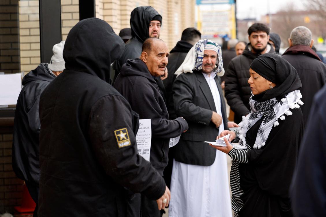Samra'a Luqman (R) hands out fliers outside of the American Moslem Society Mosque to ask voters not to vote for President Joe Biden after Friday prayers in Dearborn Heights. (AFP)