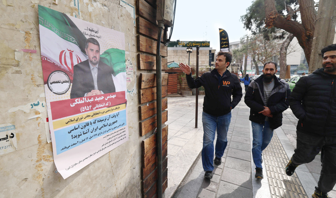 Men walk past a wall bearing an electoral campaign poster, ahead of the country’s upcoming parliamentary elections, in Tehran on Saturday. (AFP)